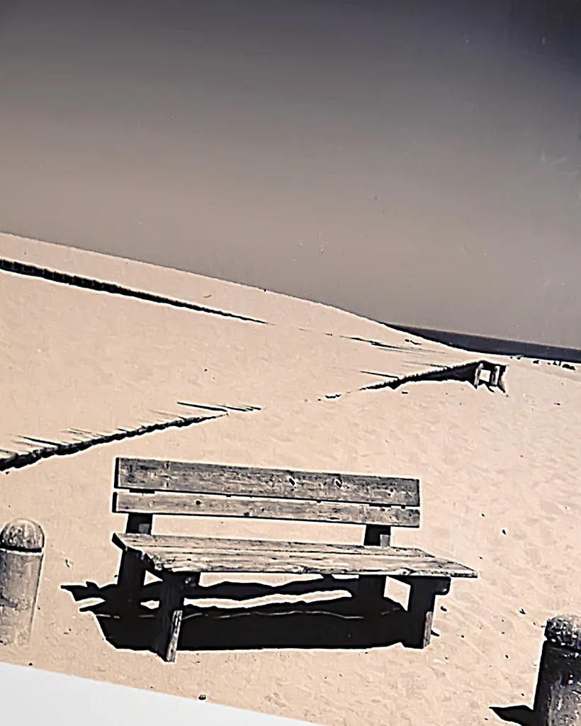 Beach Relaxation, Dan Andrei — detail of the photographic image: a wooden bench on a sand-dune boardwalk leading toward the sea.
