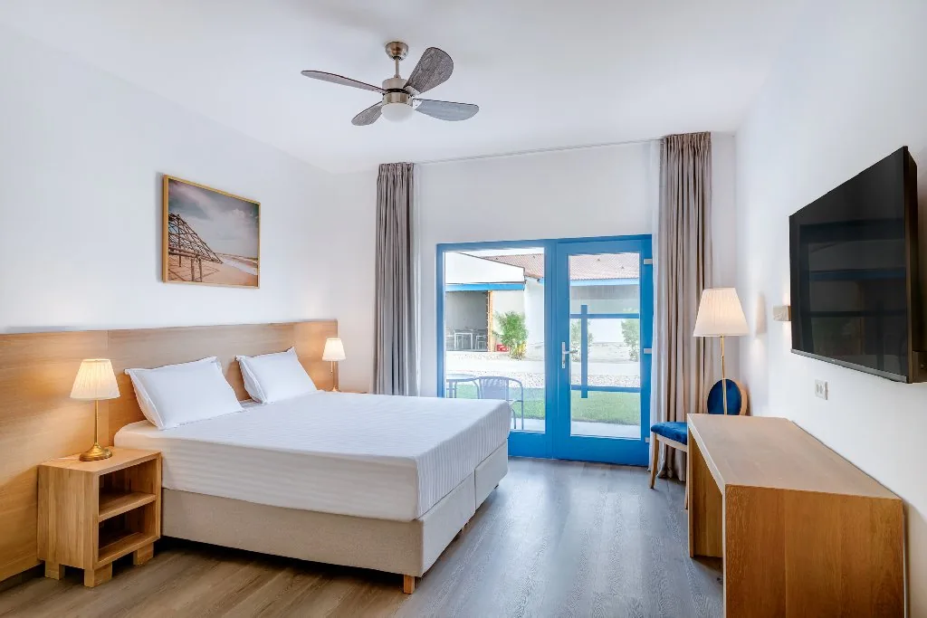 Bright hotel guestroom with a framed coastal photograph above the bed.